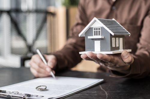 Pessoa a assinar um contrato enquanto segura uma casa em miniatura